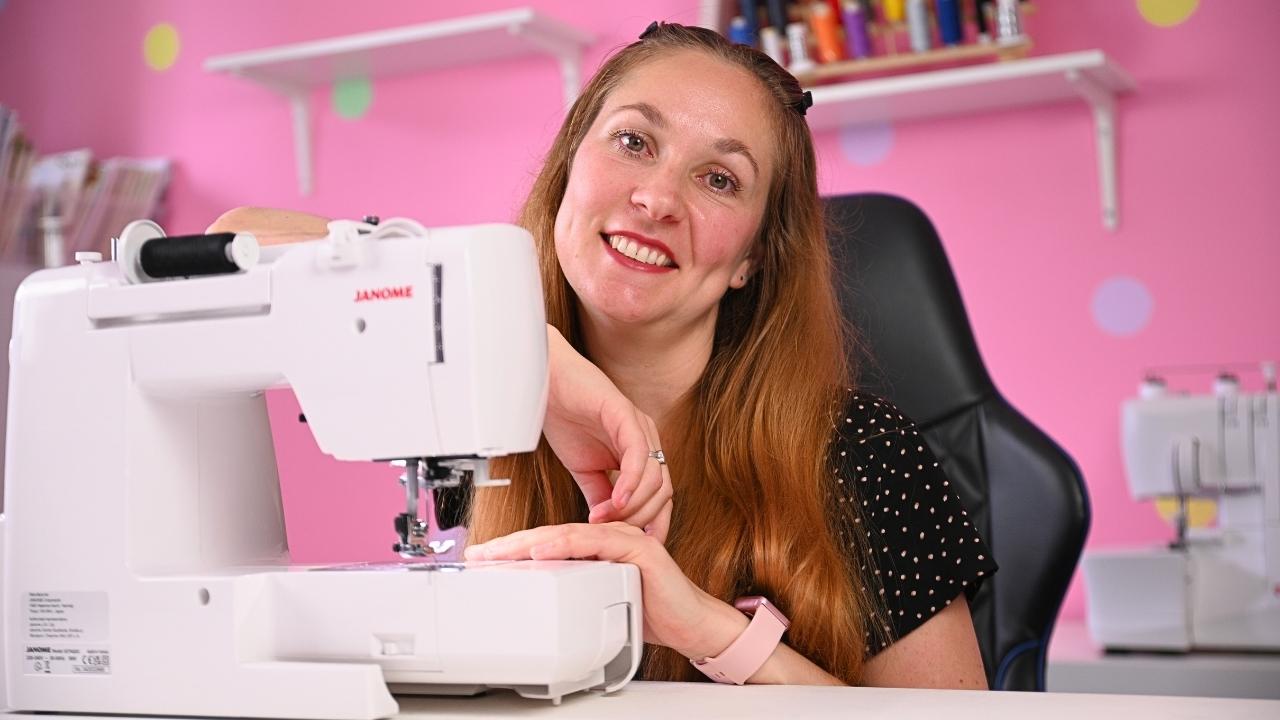 Woman using a sewing machine in a pink room with shelves.